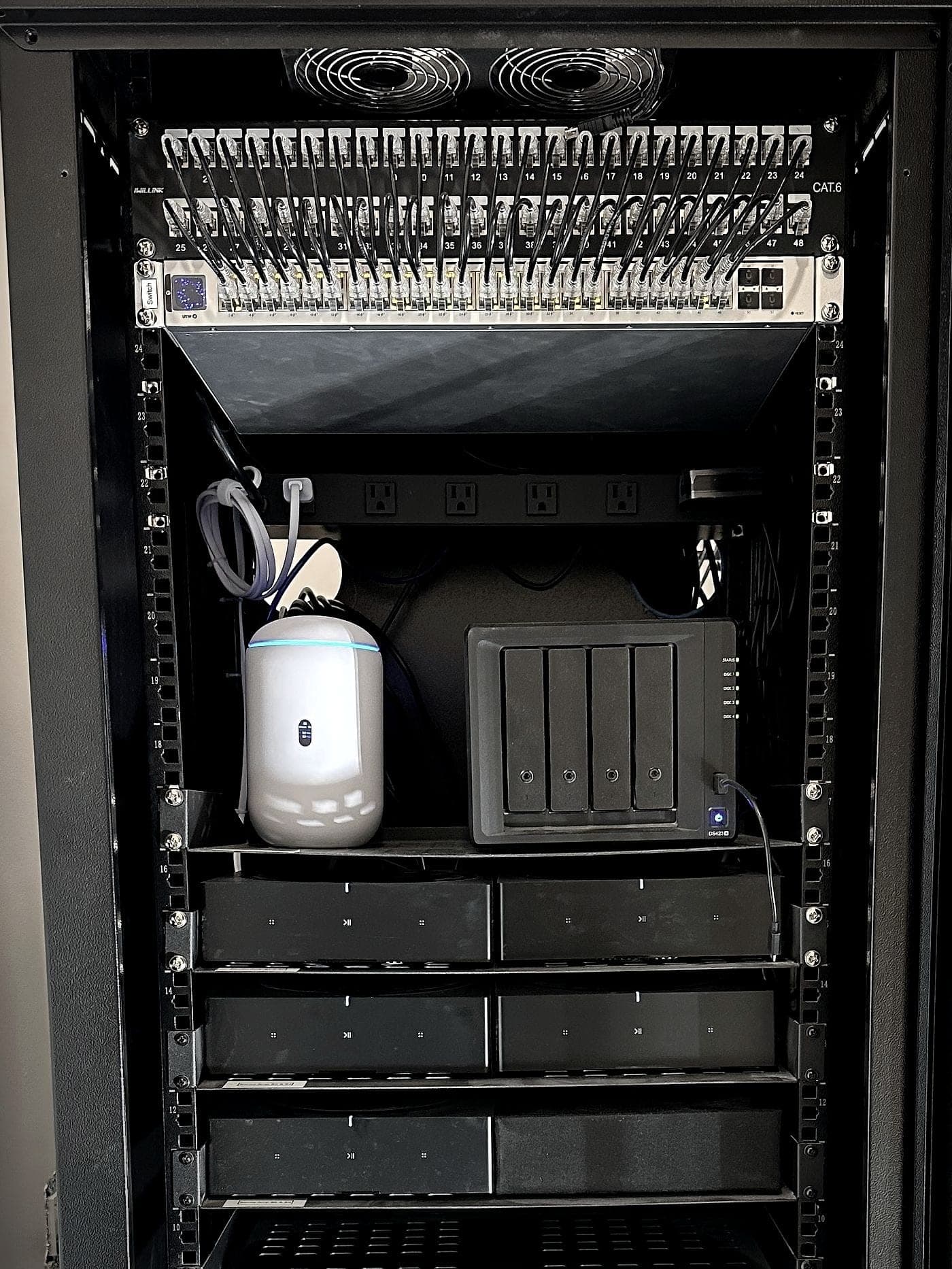 Open equipment rack: patch panels and switch at the top, the gateway and network storage, then three shelves of audio amplifiers