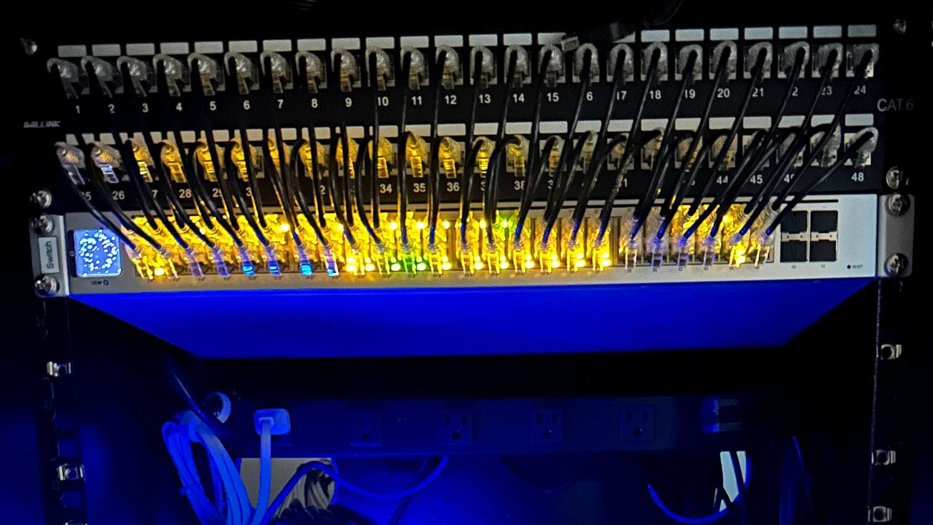 Close view of short patch cables running from the patch panels into the switch, with the ports lit